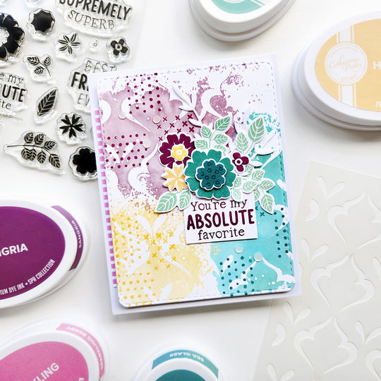 Colorful card with floral design and text, surrounded by stamping supplies on a white surface.