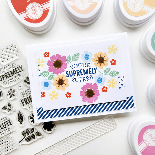 Multi-colored floral design card with text surrounded by stamping tools on a white background