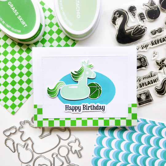 "Happy Birthday" card featuring a unicorn pool float and beach ball, set on checkered paper.