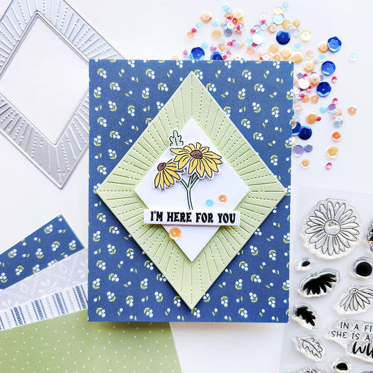 A card with the sentiment "I am here for you," featuring floral patterned paper arranged with daisies in a diamond shape, accented with sequins.