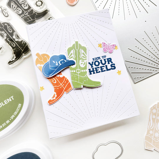A card with "Kick up your heels" sentiment, featuring a floral cowgirl hat and butterfly floral boots, set against sunray background for a western vibe!