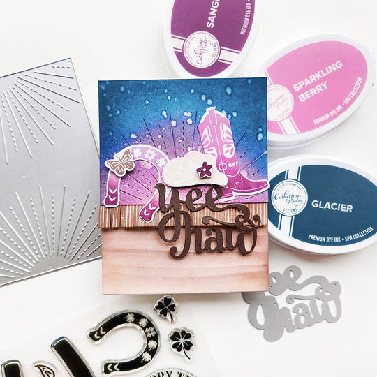 A Yeehaw card featuring a shamrock and horseshoe design, with a pink and blue ink-blended sunray. Cowgirl boots and a hat add the perfect western touch.