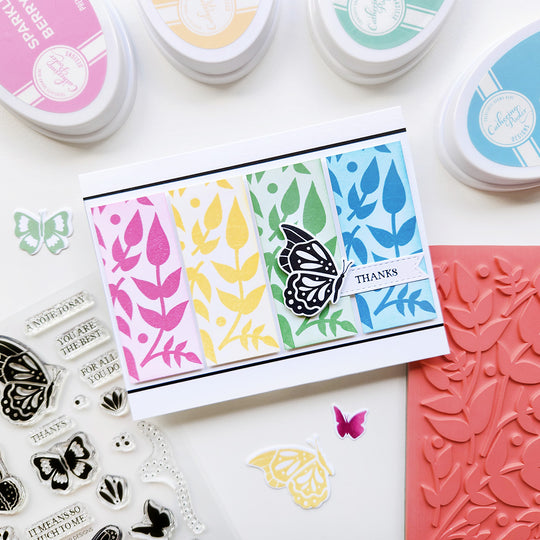 Card with butterfly and leaf patterns surrounded by stamping tools on a light background