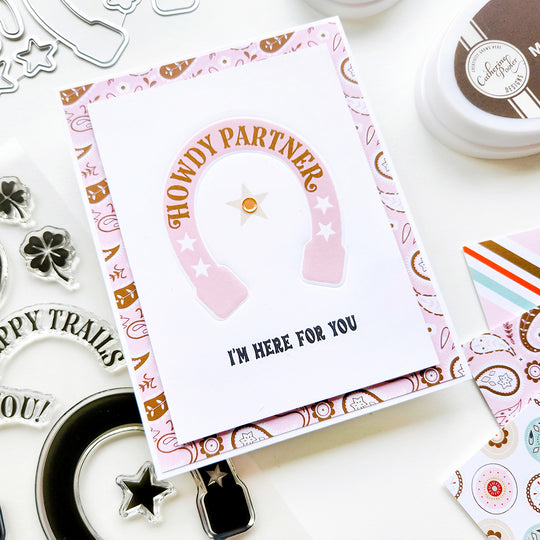 A card featuring a horseshoe and stars with the sentiment "Howdy Partner, I am here for you," crafted using paisley paper for a western design.
