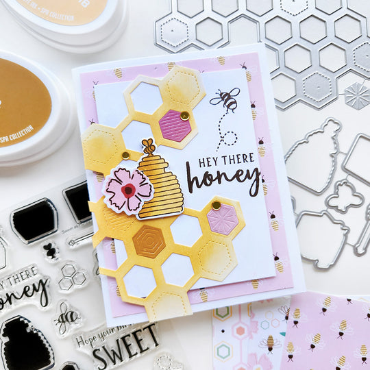 "Hey There, Honey" card with a bee, honey jar and a flower set atop honeycomb shapes, surrounded by bee-patterned paper.