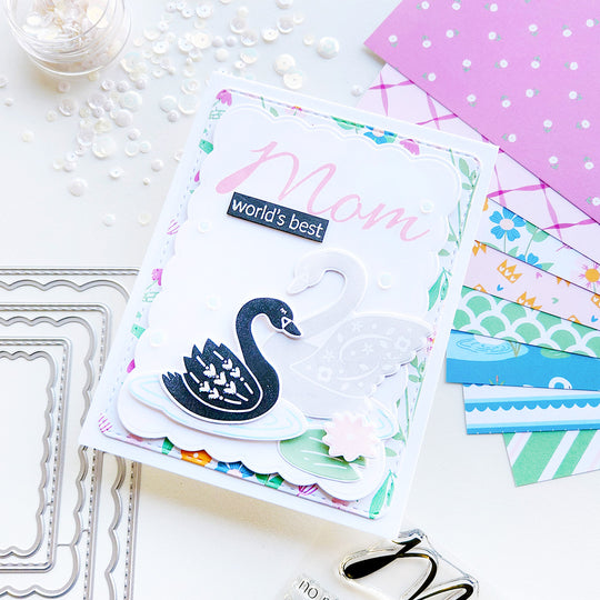 "World's Best Mom" card featuring two swans on a rippled pond with a lily pad, set against a beautiful floral-patterned paper.