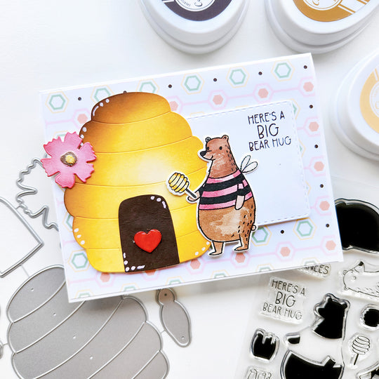"Here's a Big Bear Hug" card featuring a bear beside a beehive, with honeycomb-paper, and accented with a flower and a heart.