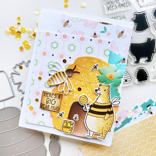 "Here's a Big Hug" card with a bear in front of a beehive, surrounded by flowers and bees, with honeycomb paper and sequin.