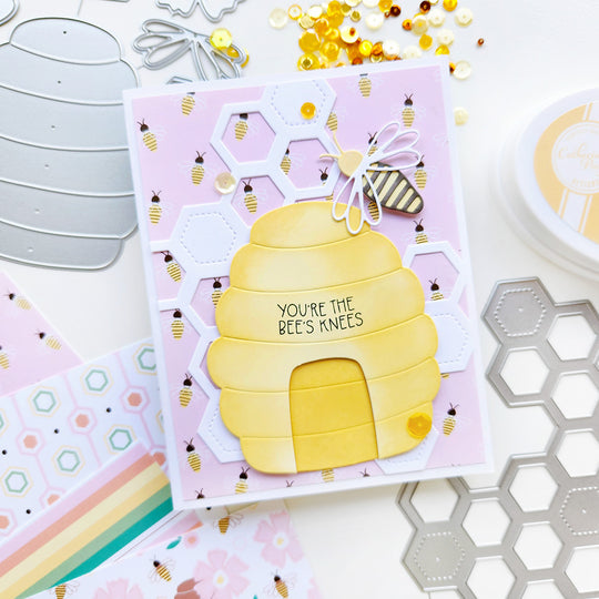 "You're the bee's knees" card with a hive and bee perched atop honeycomb shapes, set on bee-patterned paper and sequins.