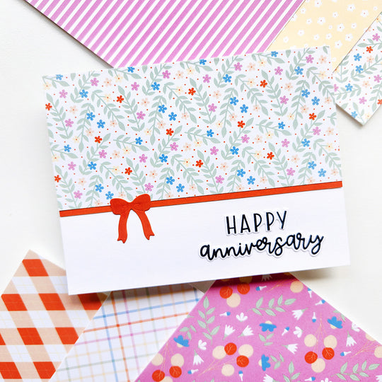 Greeting card with floral pattern, red ribbon, and 'Happy anniversary' text on a colorful background.