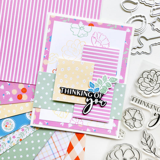 Colorful card with 'Thinking of you' text surrounded by craft materials and stamps on a white background
