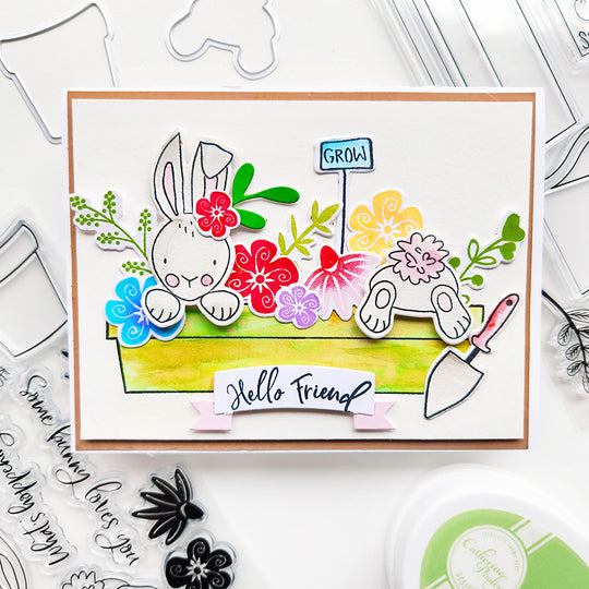 Hello, friend! Celebrate spring with this charming card featuring bunnies in a planter, surrounded by vibrant flowers.
