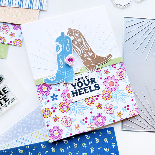 A card featuring floral and butterfly-designed cowgirl boots on a floral and sunray background, with the fun sentiment "Kick up your heels" for a western vibe!
