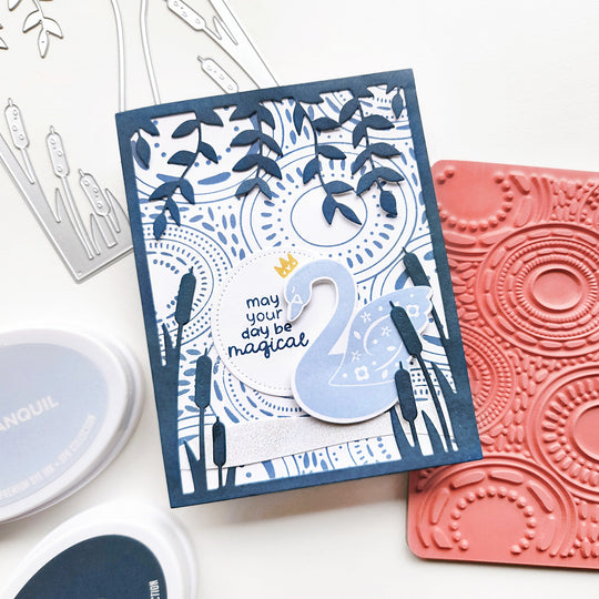 "May your day be magical" card featuring a swan on a water-rippled pond with cattails and hanging vines.