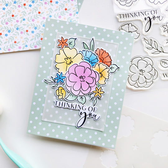 Colorful floral card with 'Thinking of you' text on a polka dot card base, surrounded by crafting tools.