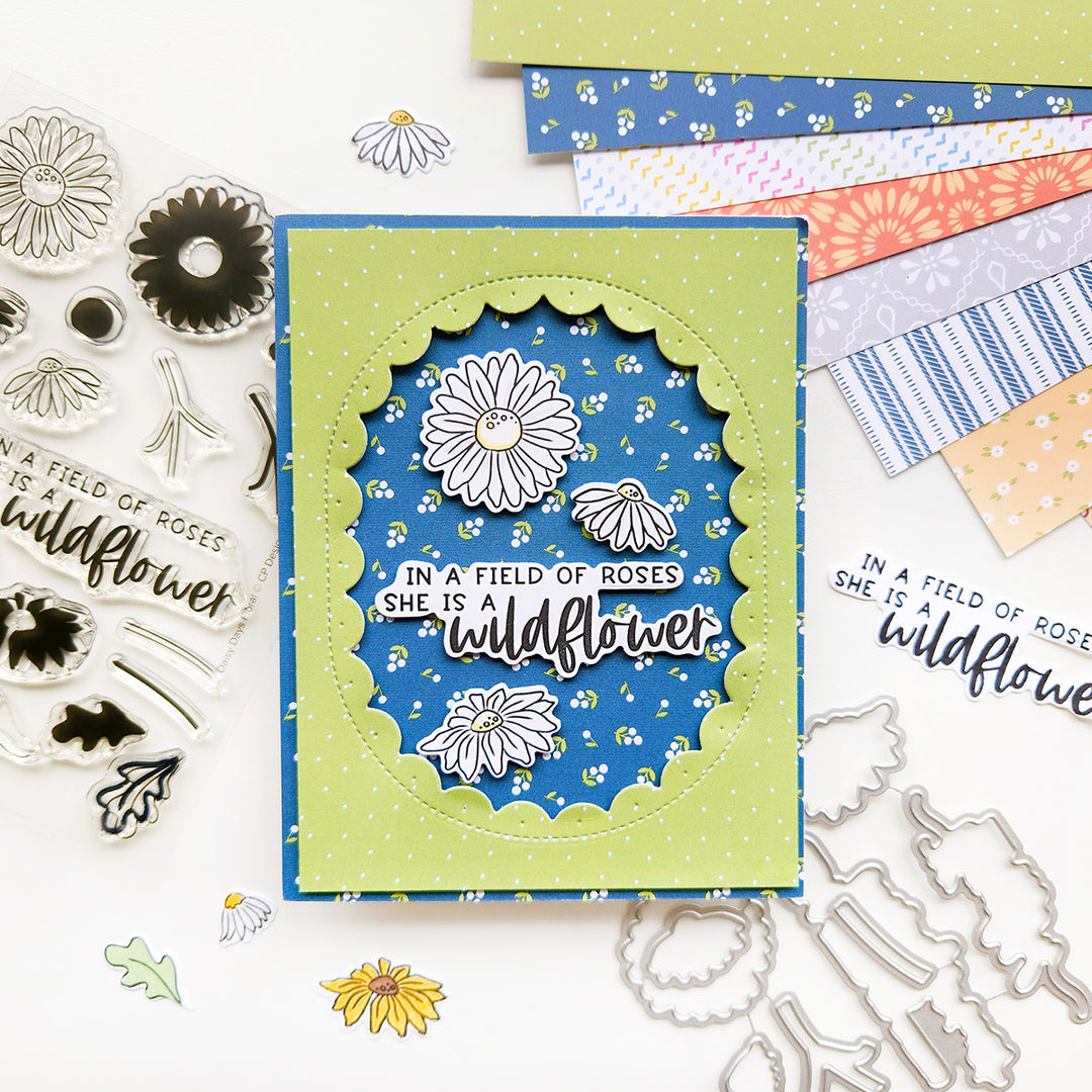 A card with the sentiment "In a field of roses, she is a wildflower," featuring daisies accents, set against green polka dot and floral-patterned paper.