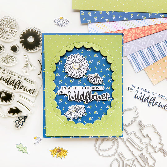 A card with the sentiment "In a field of roses, she is a wildflower," featuring daisies accents, set against green polka dot and floral-patterned paper.