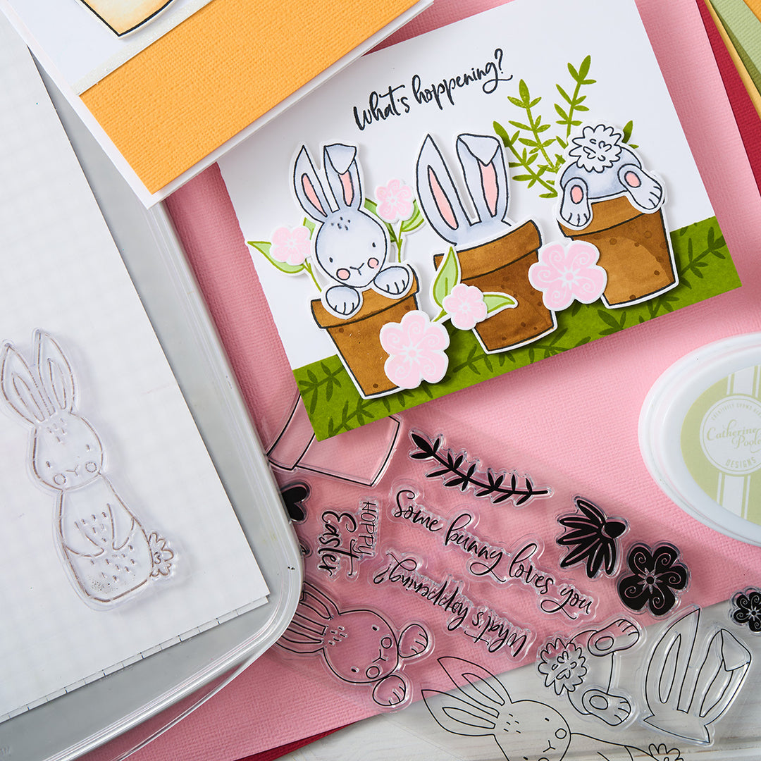 Celebrate spring with a playful what's hoppening card featuring bunnies, pink flowers, green grass, and planters.