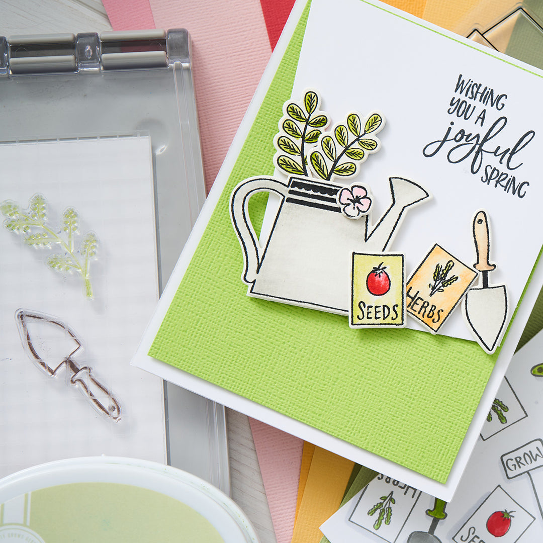 Wishing you a joyful spring! This vibrant card features a watering can, seed packs, and garden tools against a lively green background. 